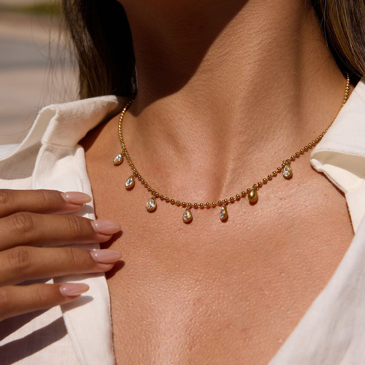 Close-up of a necklace with teardrop-shaped pendants on a person wearing a white shirt.