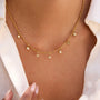 Gold necklace with small round pendants on a person wearing a white shirt.