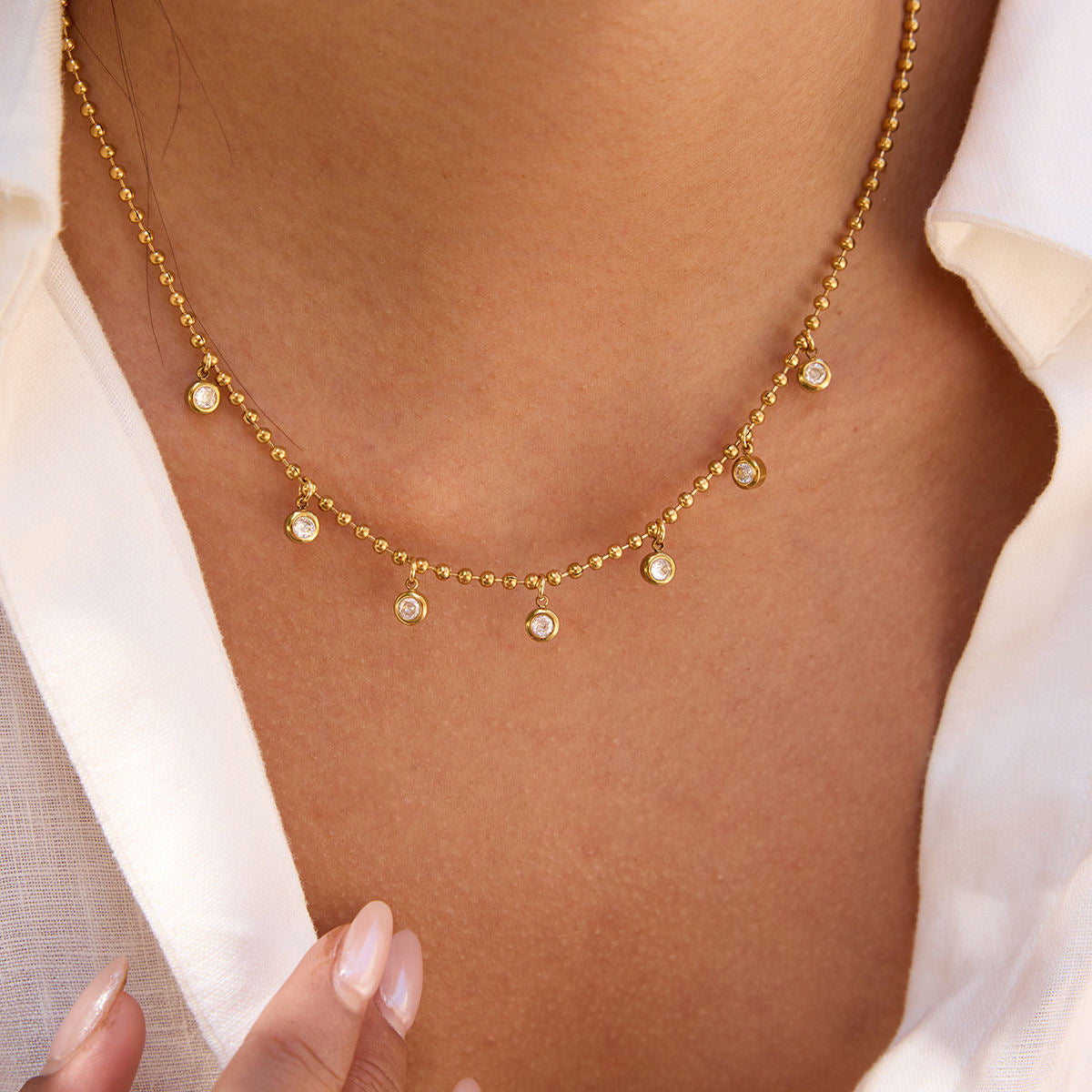 Gold necklace with small round pendants on a person wearing a white shirt.
