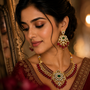 Woman wearing a traditional red and gold jewelry set with emeralds and rubies.