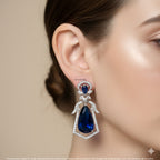 Blue teardrop earring worn by a model on a beige background