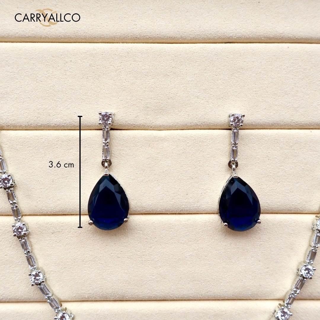 Teardrop-shaped black gemstone earrings with silver accents on a wooden surface, featuring the brand 'CARRYALICO'.