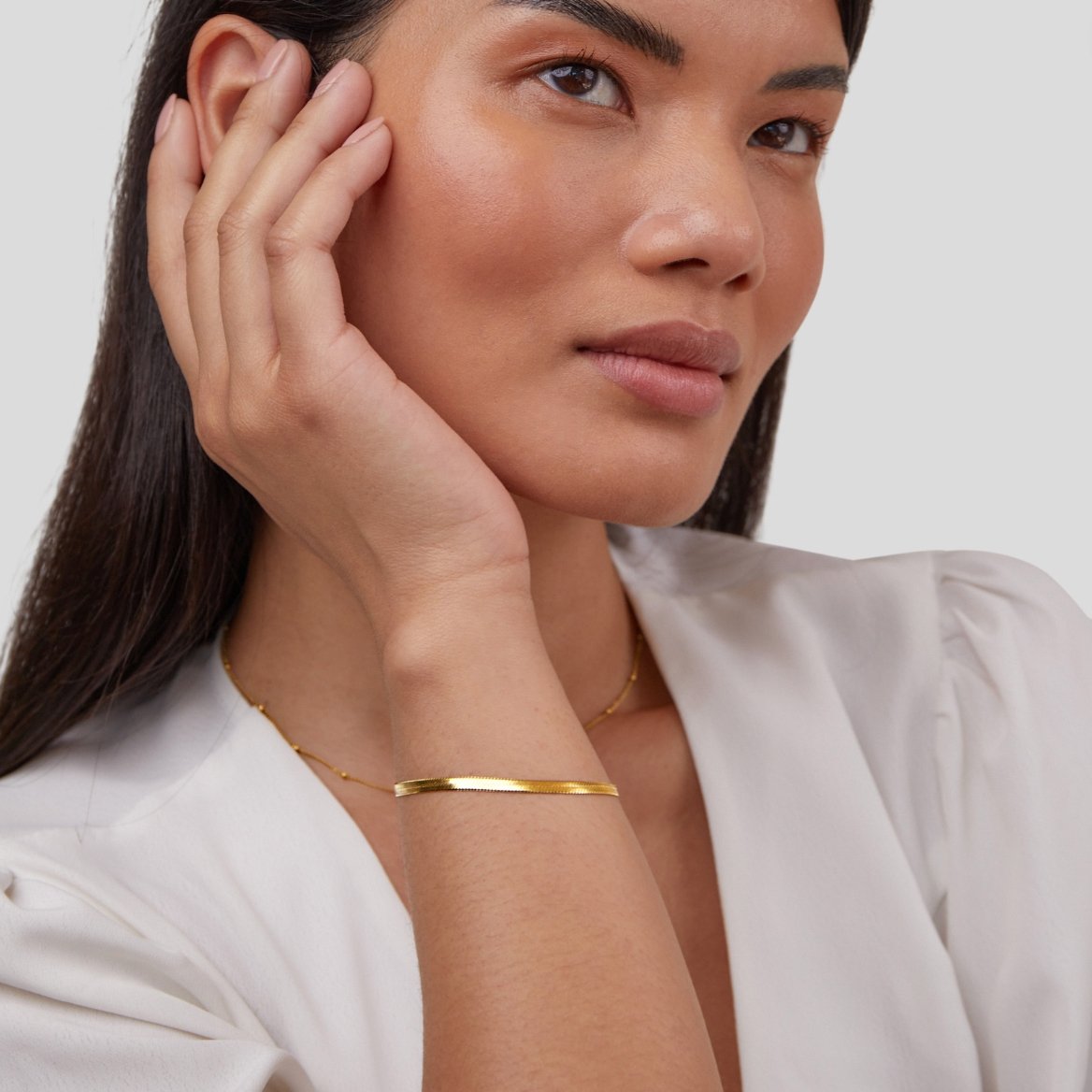 Woman wearing a gold bracelet on a plain background