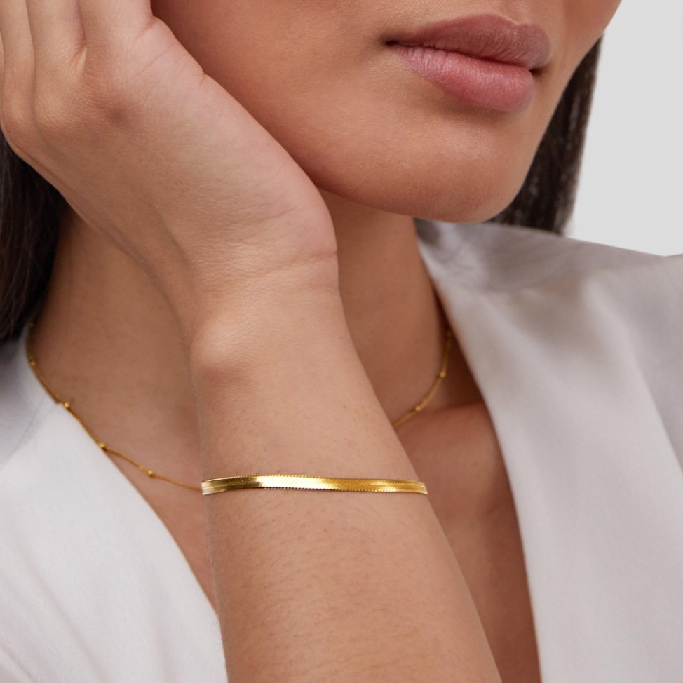 Close-up of a person wearing a gold bracelet on a plain background