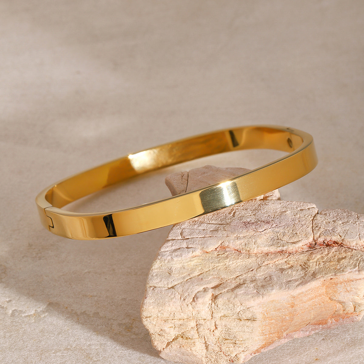 Gold bracelet on a textured stone surface with a neutral background