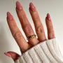Hand with pink nail polish wearing a gold ring on a neutral background