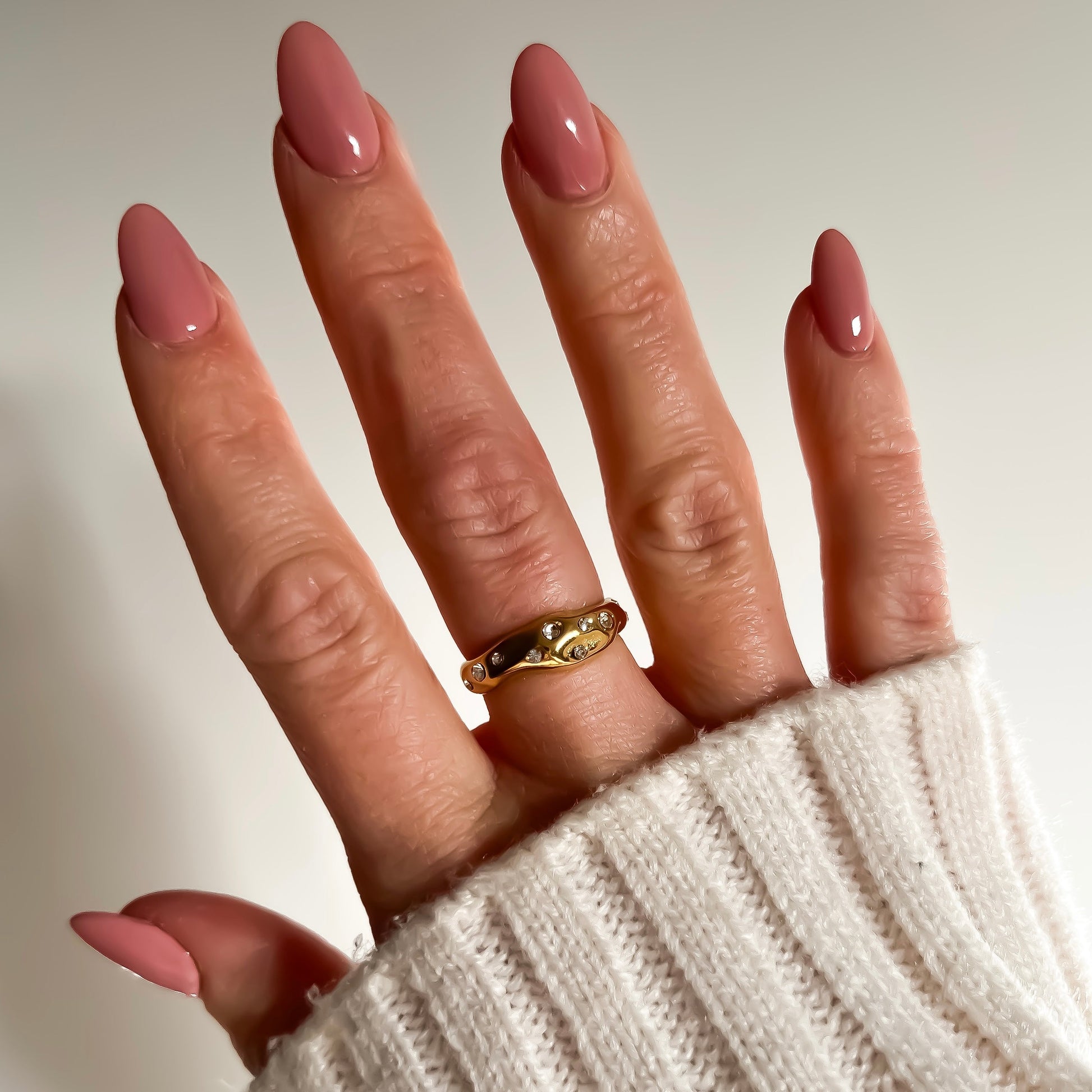 Hand with pink nail polish wearing a gold ring on a neutral background