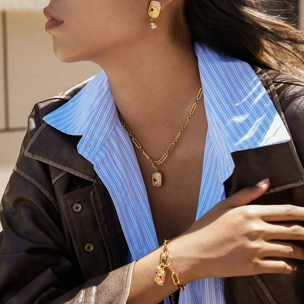 Close-up of a person wearing gold jewelry including an earring, necklace, and bracelet.