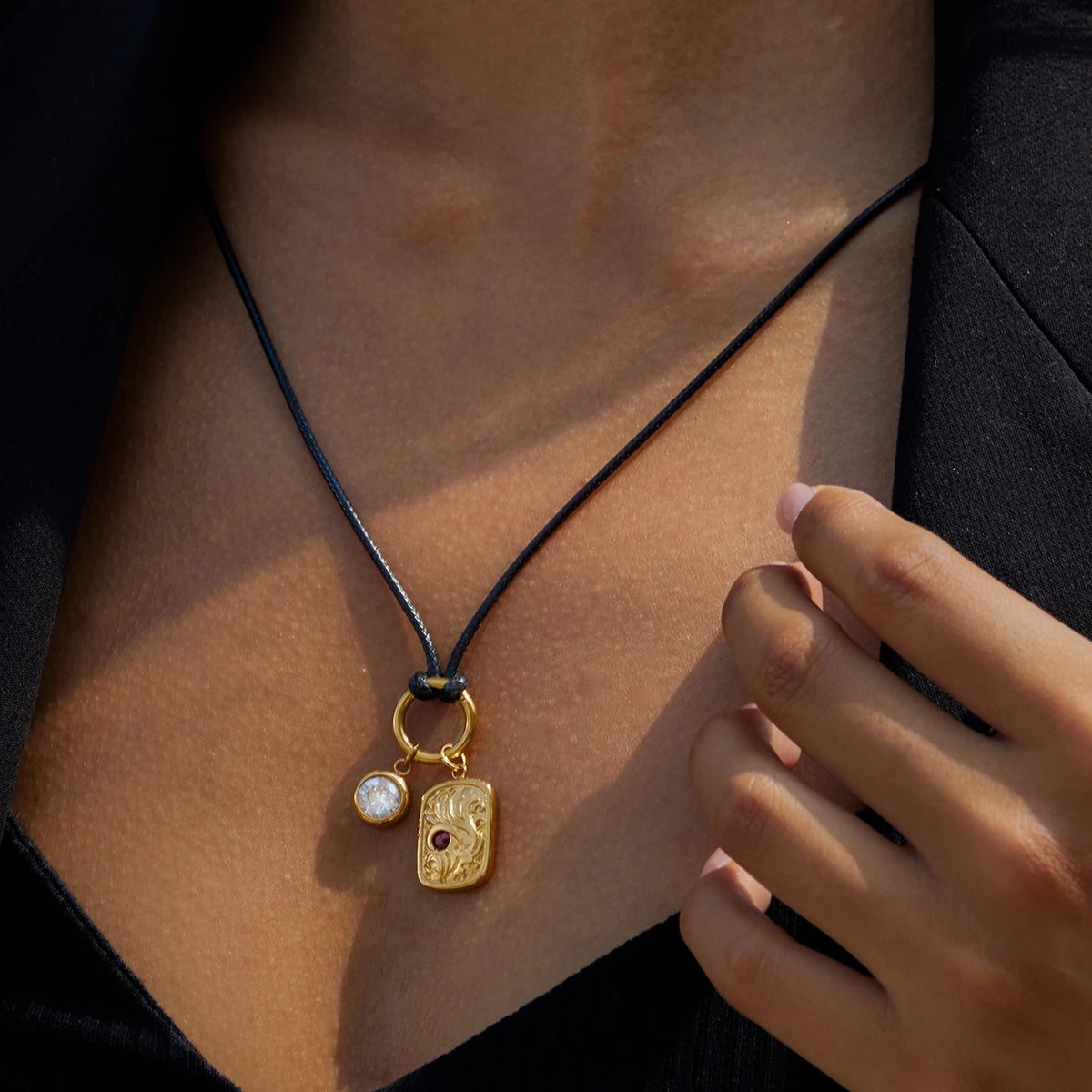 Necklace with gold pendant and black cord worn by a person