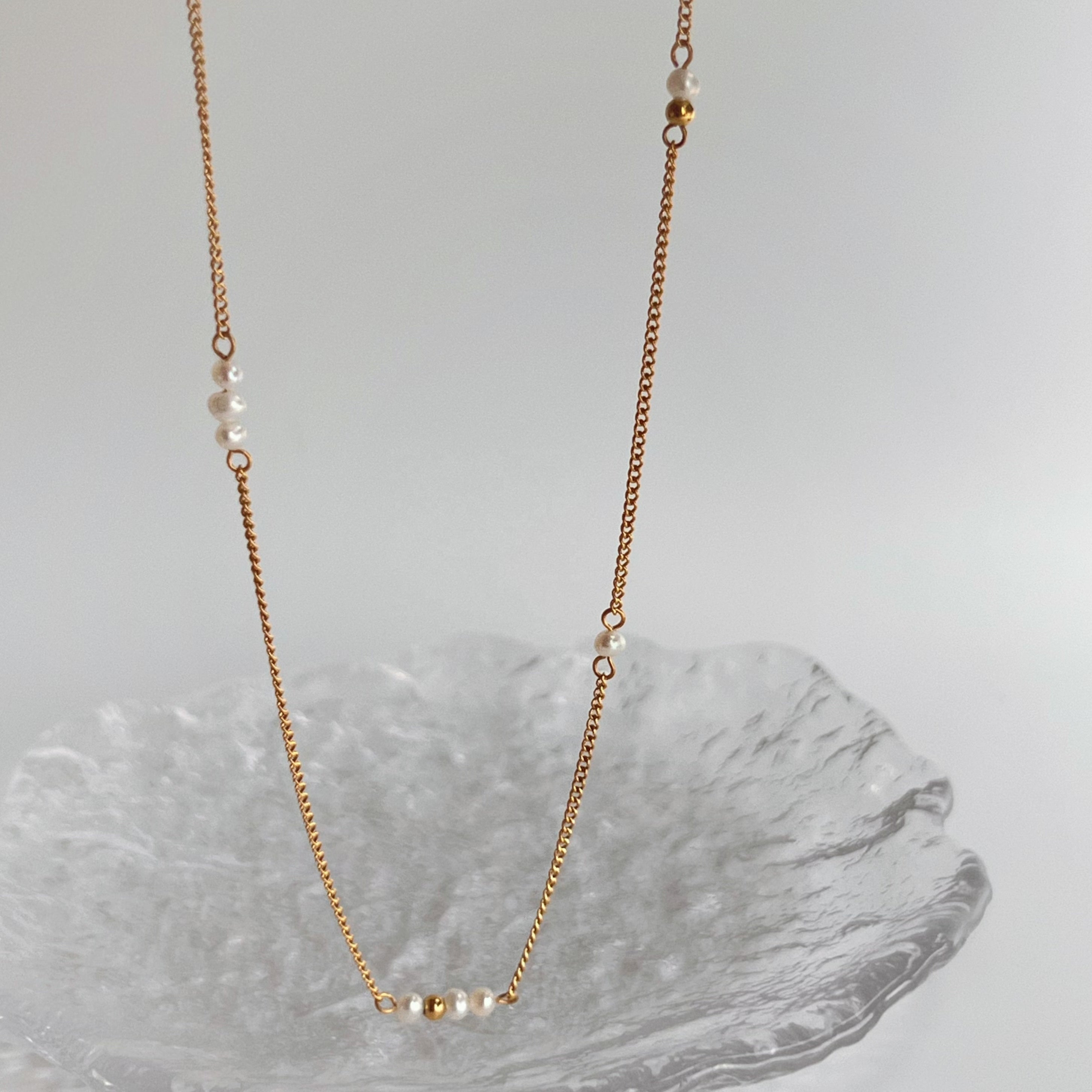 Gold chain necklace with small beads on a gray surface