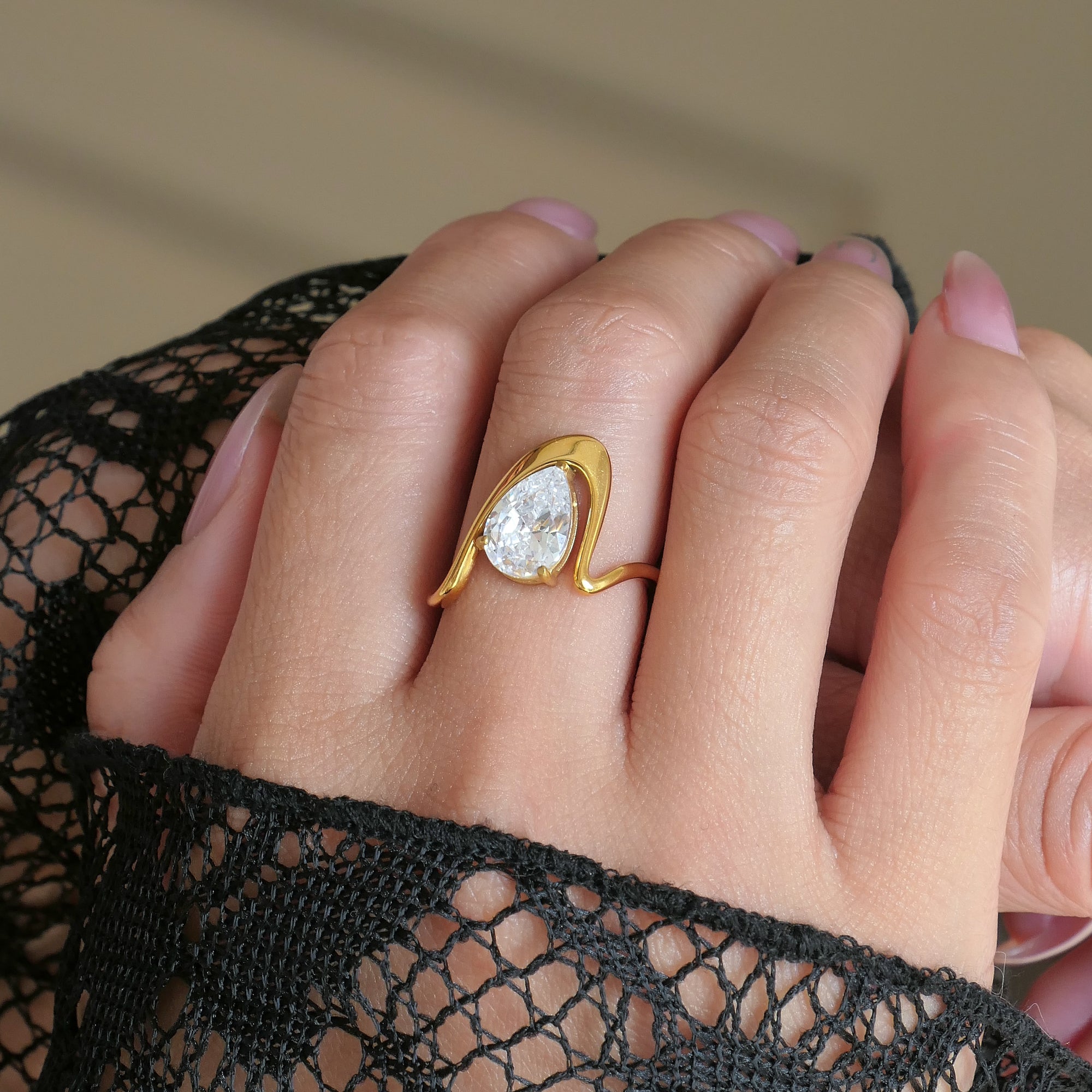 Gold ring with a large diamond on a hand wearing black lace gloves.