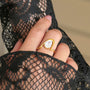 Hand wearing a gold ring with a clear gemstone on black lace fabric