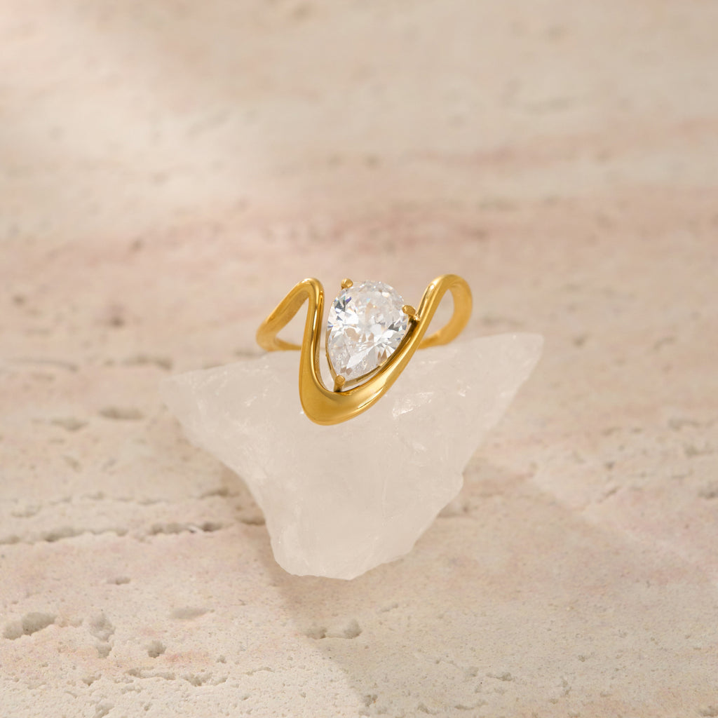Gold ring with a pear-shaped diamond on a textured beige surface