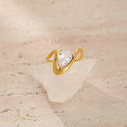 Gold ring with a pear-shaped diamond on a textured beige surface
