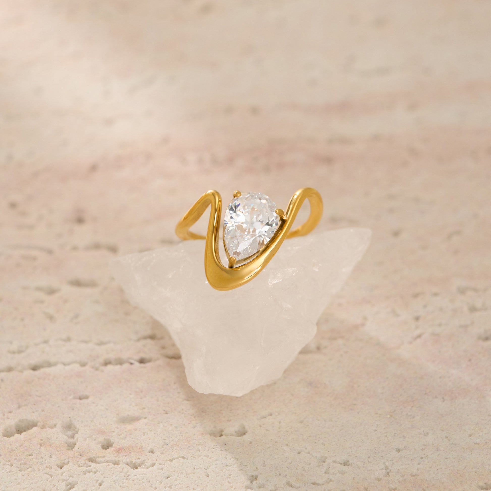 Gold ring with a pear-shaped diamond on a textured beige surface