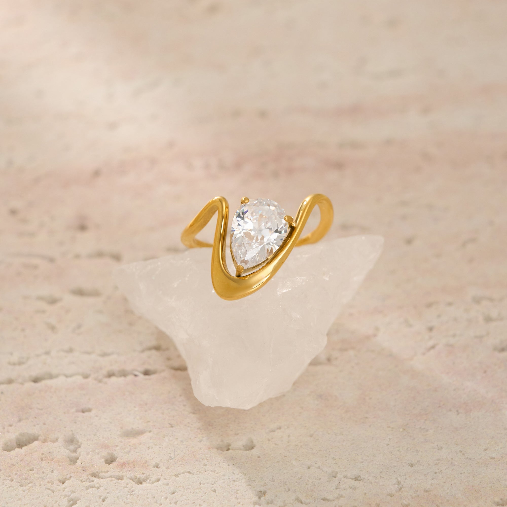 Gold ring with a pear-shaped diamond on a textured beige surface