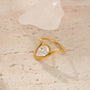 Gold ring with a heart-shaped diamond on a textured beige surface