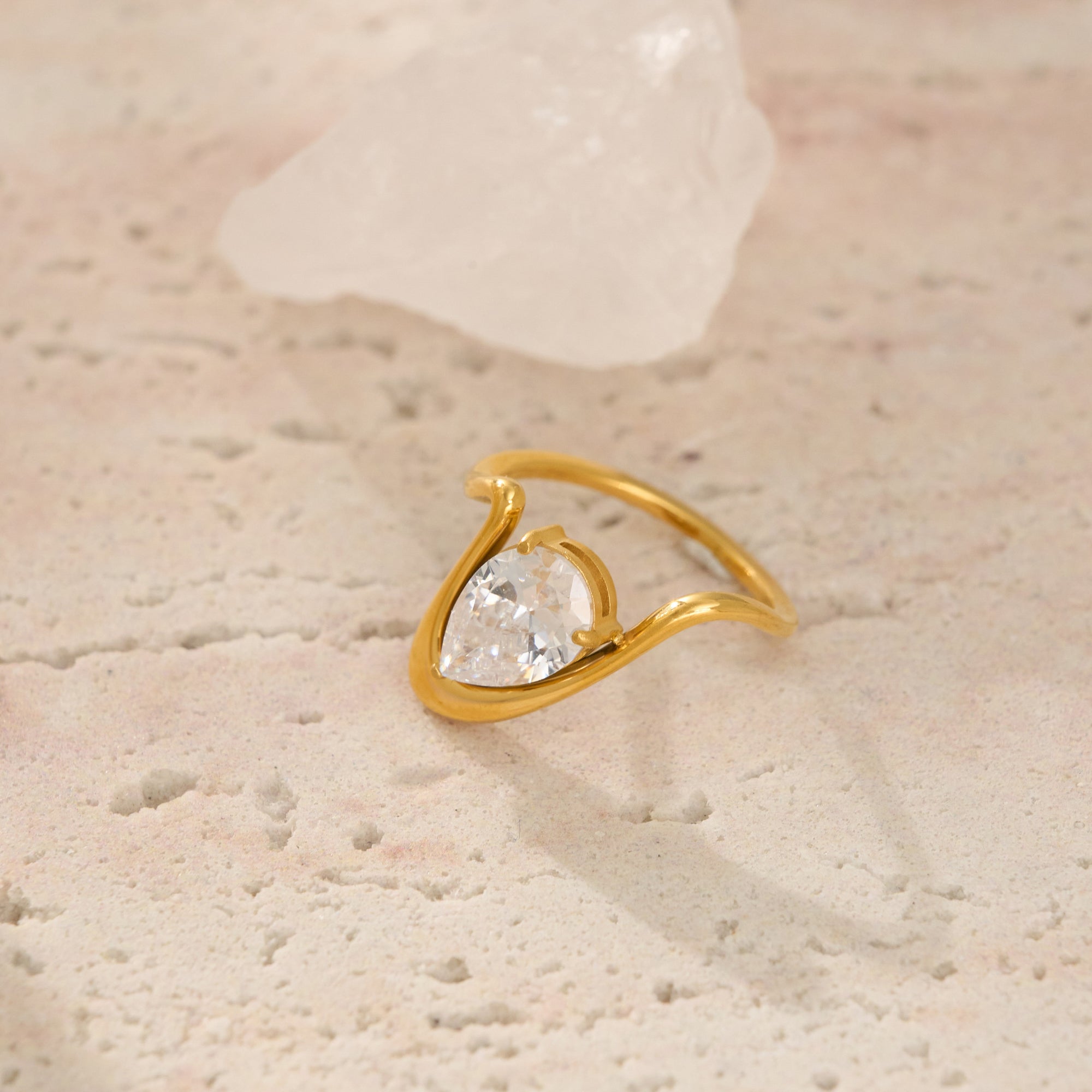 Gold ring with a heart-shaped diamond on a textured beige surface