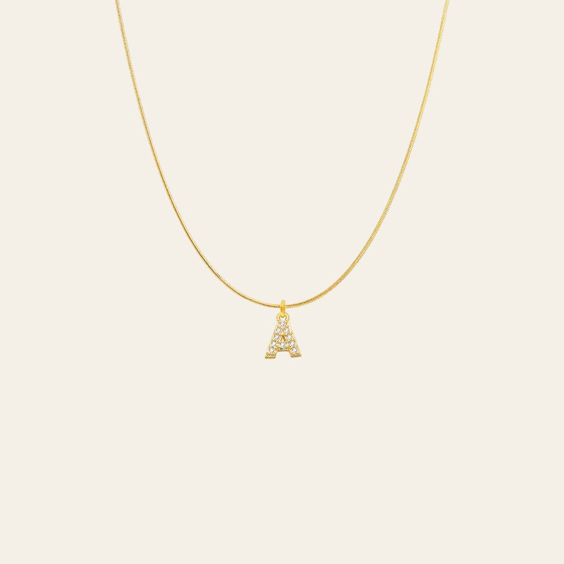 A delicate gold chain necklace featuring a small pendant shaped like the letter 'A', embellished with small clear stones, shown against a plain white background.