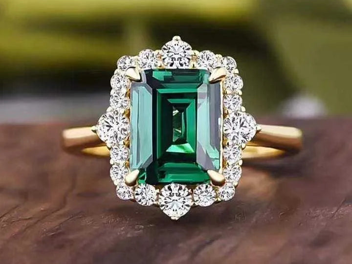 Gold ring with a green gemstone and diamond accents on a wooden surface