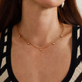 Gold necklace with small pearls on a person wearing a black and white striped top.