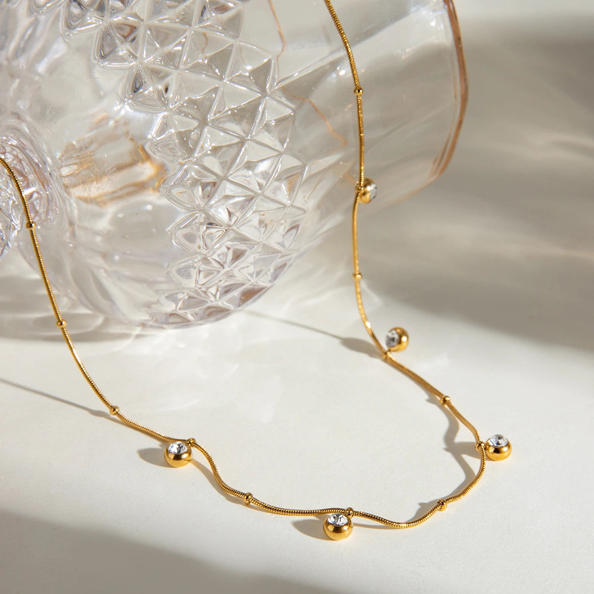 Gold necklace with small spherical pendants on a light background