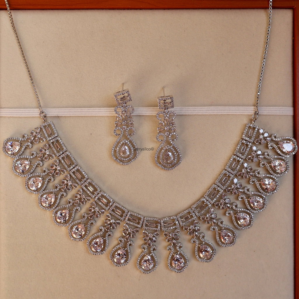 Silver necklace and earrings set on a beige background